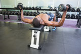 Shirtless man exercising with dumbbells in gym
