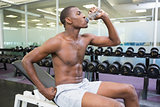 Side view of shirtless man drinking water at gym