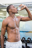 Shirtless man drinking water at gym