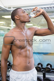Shirtless man drinking water at gym