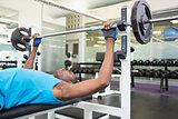 Determined young man lifting barbell in gym