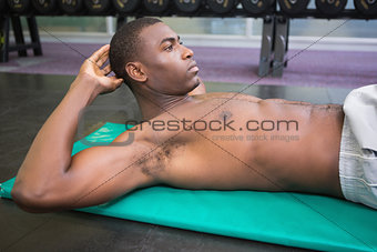 Shirtless man doing abdominal crunches in gym