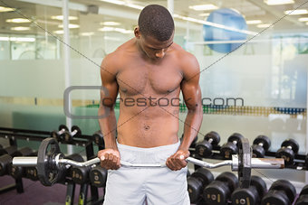Shirtless man lifting barbell in gym