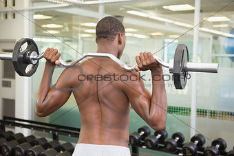 Rear view of shirtless man lifting barbell in gym
