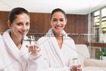 Smiling women in bathrobes drinking water