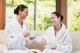 Smiling women in bathrobes having tea