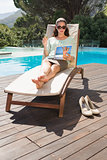 Woman reading book on sun lounger by pool
