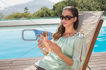 Woman reading book on sun lounger by pool
