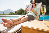 Woman reading book by pool with champagne in foreground
