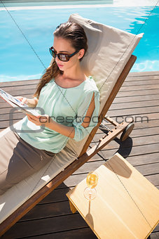 Woman reading book by swimming pool with champagne on table
