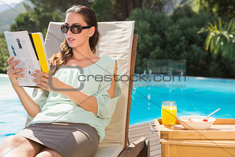 Woman reading book by pool with breakfast on table
