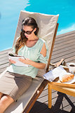 Woman reading book by pool with breakfast on table