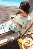 Woman drinking tea by pool with breakfast on table