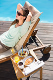 Woman relaxing by pool with breakfast on table
