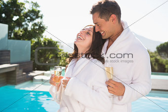 Cheerful couple with champagne flutes by swimming pool