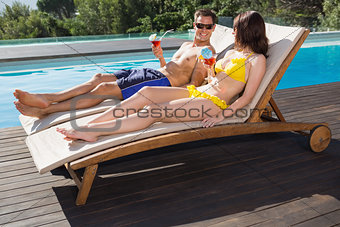 Couple with drinks sitting by swimming pool