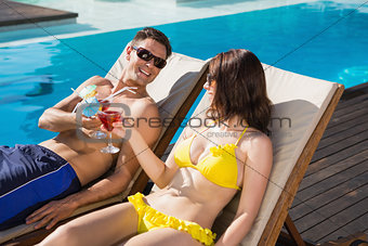 Couple toasting drinks by swimming pool