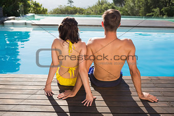 Rear view of couple sitting by swimming pool