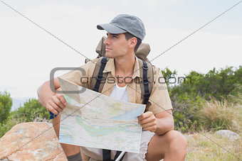 Hiking man sitting with map on mountain terrain