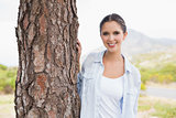 Smiling young woman by tree trunk