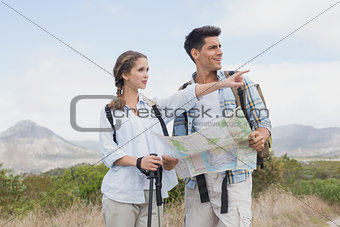 Hiking couple with map pointing ahead on mountain terrain