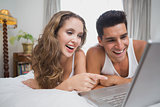 Cheerful couple using laptop in bed at home