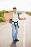 Cheerful man hitchhiking with cardboard on countryside road