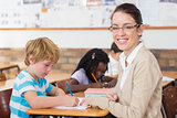Pretty teacher helping pupil in classroom smiling at camera