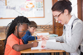 Cute pupil getting help from teacher in classroom