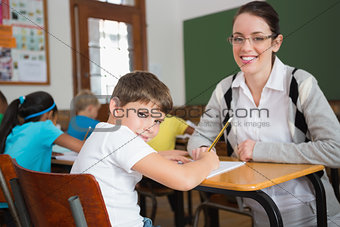 Pretty teacher helping pupil in classroom smiling at camera