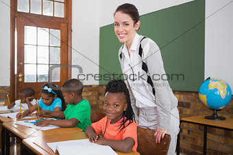 Cute pupil and teacher smiling at camera in classroom