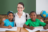 Cute pupils and teacher smiling at camera in classroom