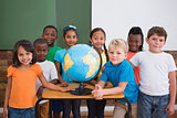 Cute pupils smiling at camera in classroom with globe
