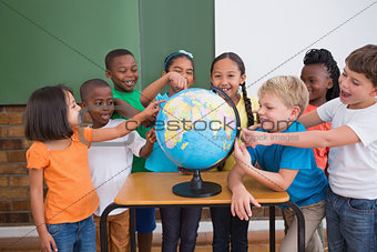Cute pupils pointing to globe in classroom