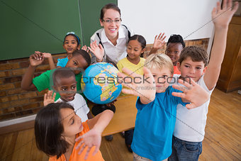 Cute pupils smiling around a globe in classroom with teacher