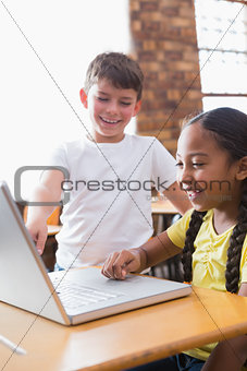 Cute little pupils looking at laptop in classroom