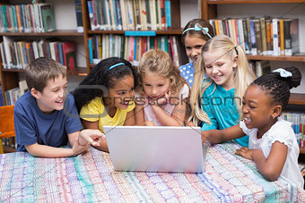Cute pupils looking at laptop in library