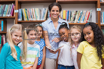 Cute pupils and teacher reading book in library