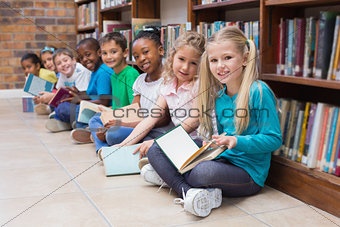 Cute pupils sitting on floor in library