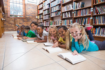 Cute pupils and teacher lying on floor in library