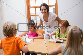 Pretty teacher standing with pupils at desk