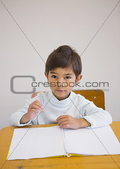 Pupil writing in notepad at his desk smiling at camera