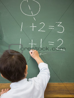 Cute pupil writing maths on chalkboard