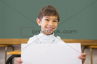 Cute pupil smiling at camera in classroom showing page