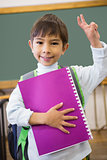 Cute pupil smiling at camera in classroom holding notepad