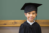 Cute pupil in graduation robe smiling at camera in classroom