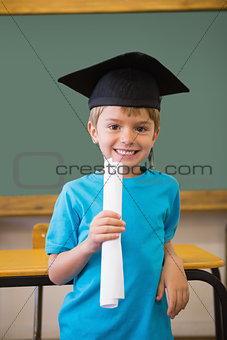 Cute pupil in mortar board smiling at camera in classroom