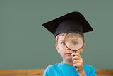 Cute pupil in mortar board smiling at camera in classroom