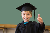 Cute pupil in graduation robe smiling at camera in classroom