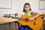 Cute pupil playing guitar in classroom